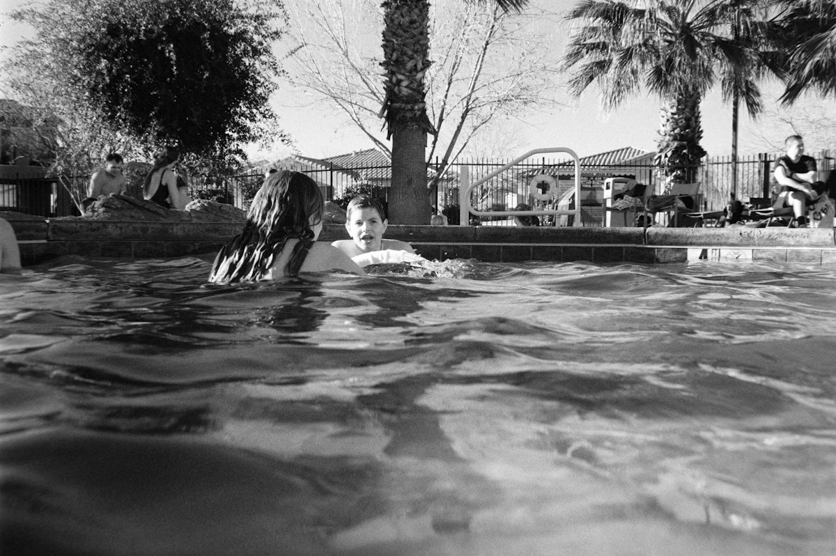 Duas pessoas nadando em piscina com palmeiras
